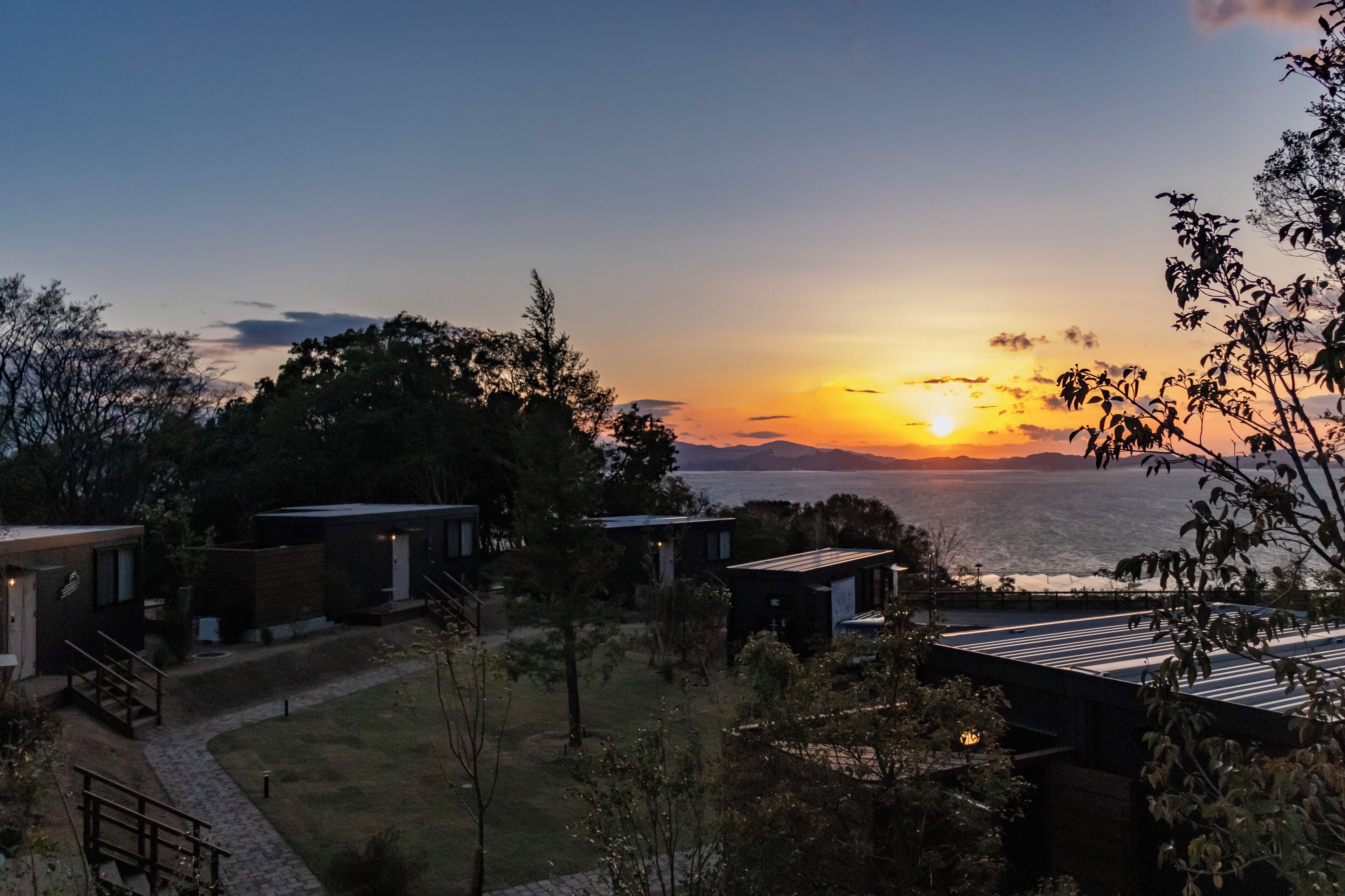 Un resort con edificios modernos, un camino hacia la playa y vistas al atardecer.