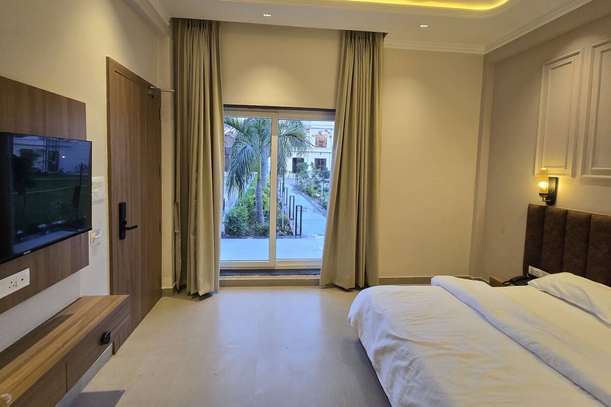A hotel room with a bed, a TV mounted on the wall, a window with curtains, and a view of the outside.