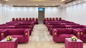 A conference room with rows of red velvet chairs and matching ottomans, a polished marble floor, and a door at the front.
