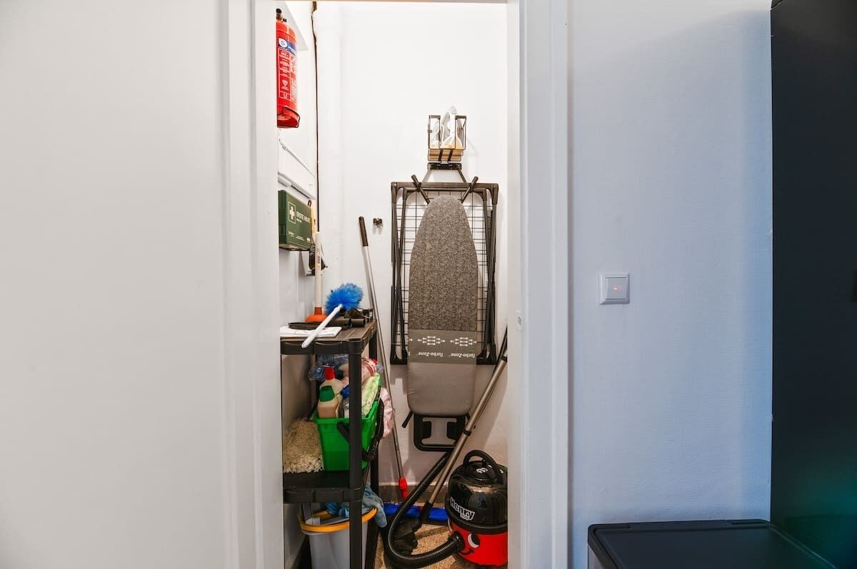 A narrow hallway with a laundry basket, cleaning supplies, and a vacuum cleaner.