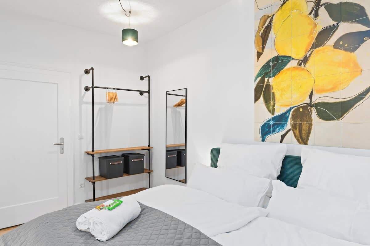 A modern hotel room with a bed, a wardrobe, a mirror, and a wall art of lemons.