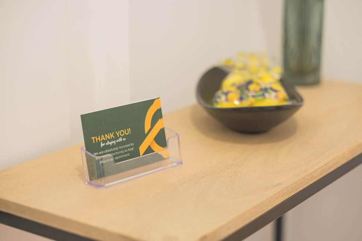 A thank you card on a clear stand, a bowl of snacks, and a vase on a wooden table.