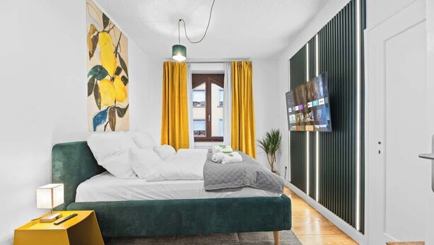 A modern bedroom with a green bed, white bedding, a painting, a TV, and a yellow curtain. - Central Karlsruhe Apt: Balcony, Fast WiFi (Karlsruhe)