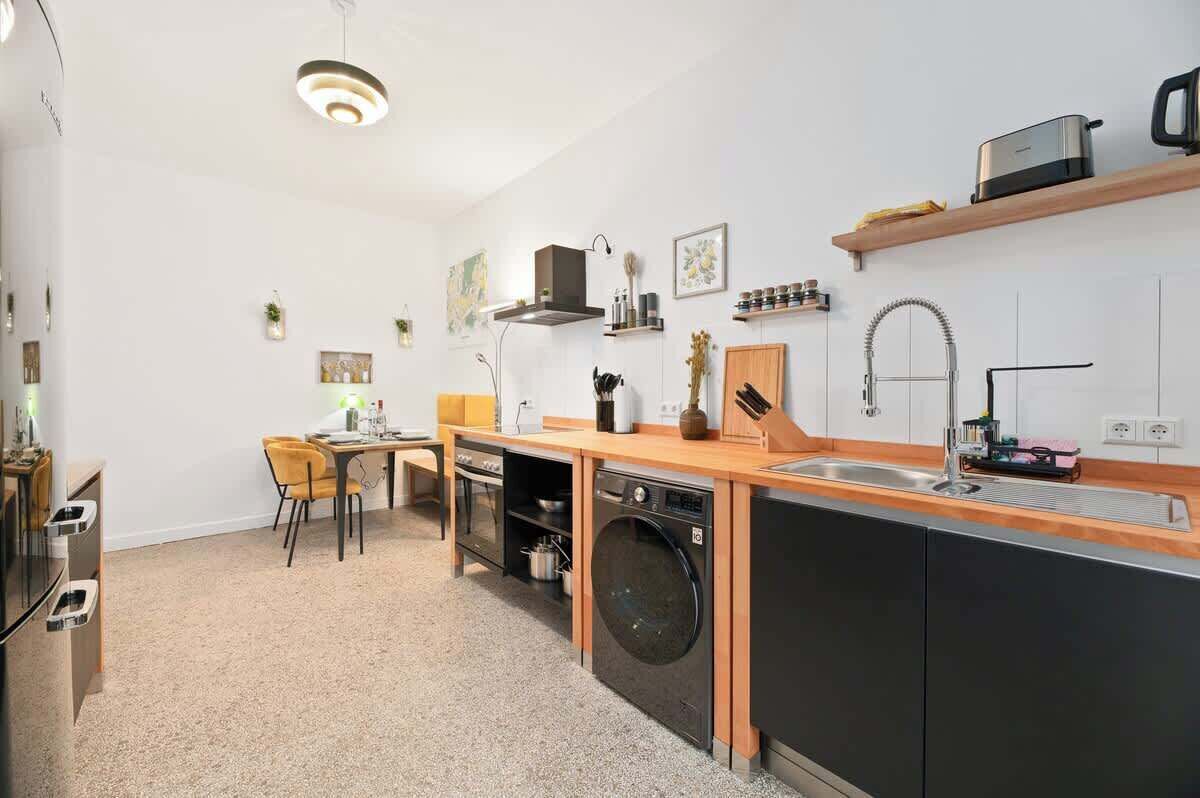 A compact kitchen with a built-in washer and dryer, a wooden countertop, and a small dining area with a chair.