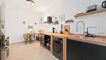 A compact kitchen with a built-in washer and dryer, a wooden countertop, and a small dining area with a chair.