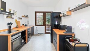 A compact kitchen with a built-in oven, a refrigerator, and a coffee machine. There is a window providing natural light and a view of the outside. - Central Karlsruhe Apt: Balcony, Fast WiFi (Karlsruhe)
