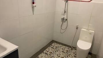 Un baño pequeño con paredes de azulejos blancos, piso de mosaico, inodoro y ducha con una tubería roja.
