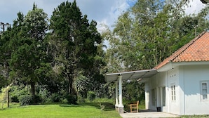 A white house with a tiled roof, a stone pathway leading to a covered porch, and lush greenery surrounding the property. - BADAI HERITAGE VILLA KALIURANG (Pakem)