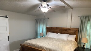 A bedroom with a wooden bed, a ceiling fan, two bedside lamps, and light blue curtains. - 3-bedroom house on Eufaula Lake in delightful Porum (Porum)