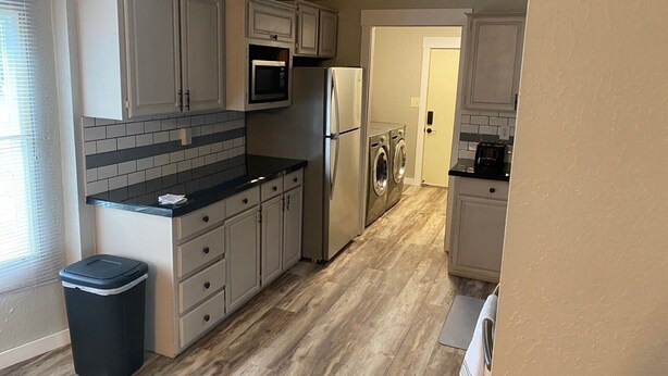 A compact kitchen with white cabinets, a black countertop, a microwave, a refrigerator, and a washing machine. - 3-bedroom house on Eufaula Lake in delightful Porum (Porum)