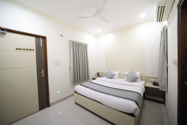A bedroom with a bed, bedside tables, a ceiling fan, and a door. - Hari Haran Prestige (Varanasi)