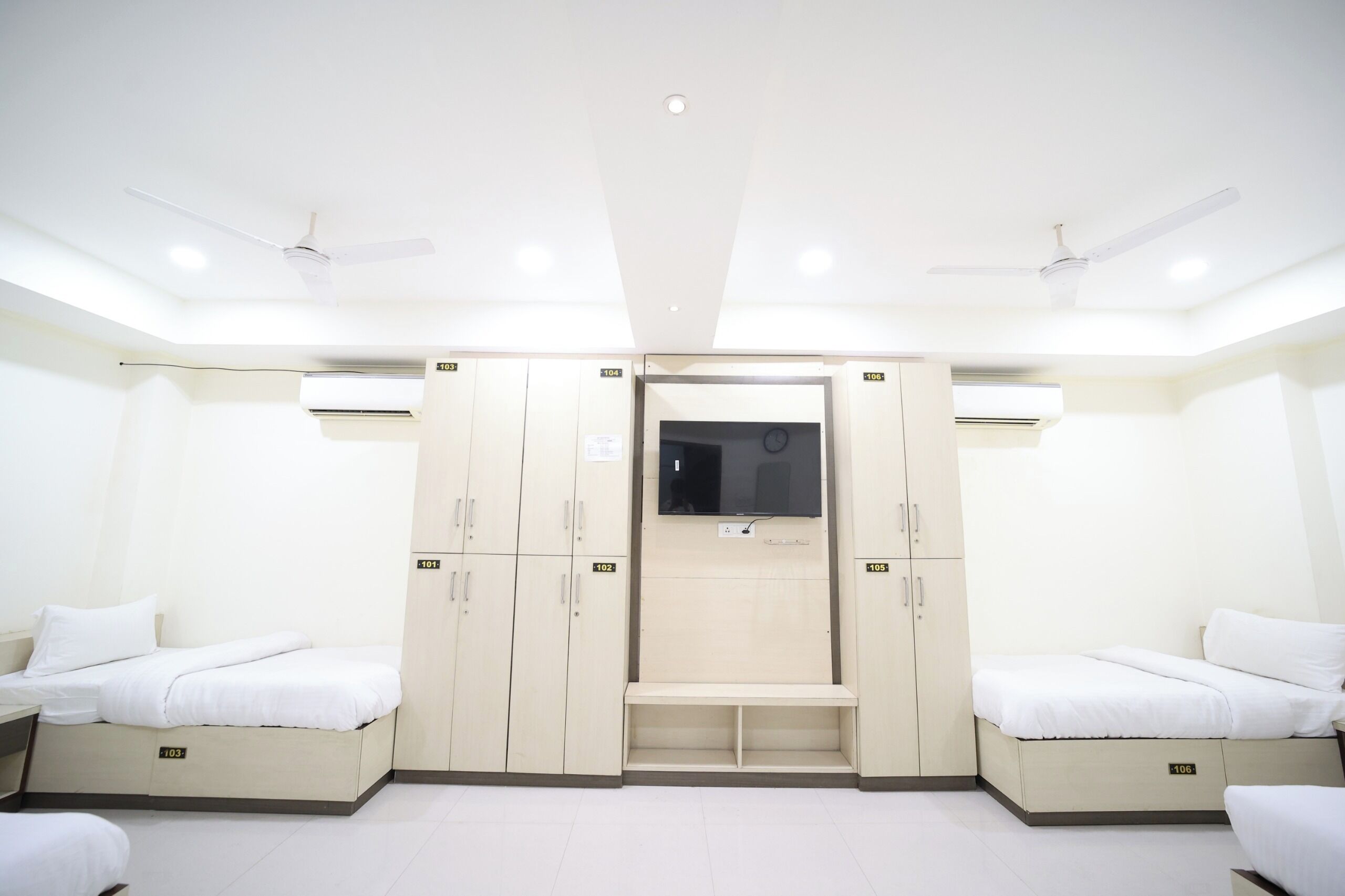 A hotel room with two beds, a wardrobe, a television, and ceiling fans.