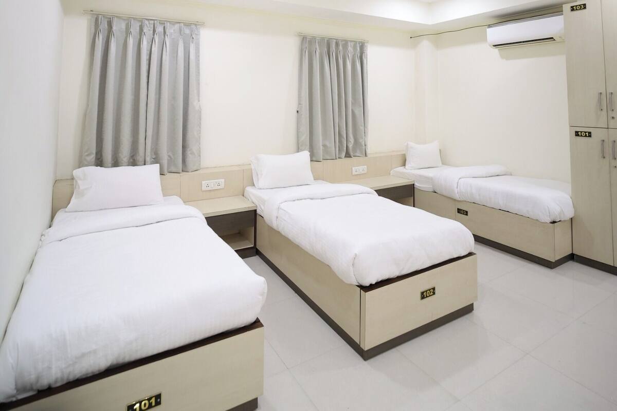 A hotel room with three single beds, a ceiling fan, an air conditioning unit, and a skylight.
