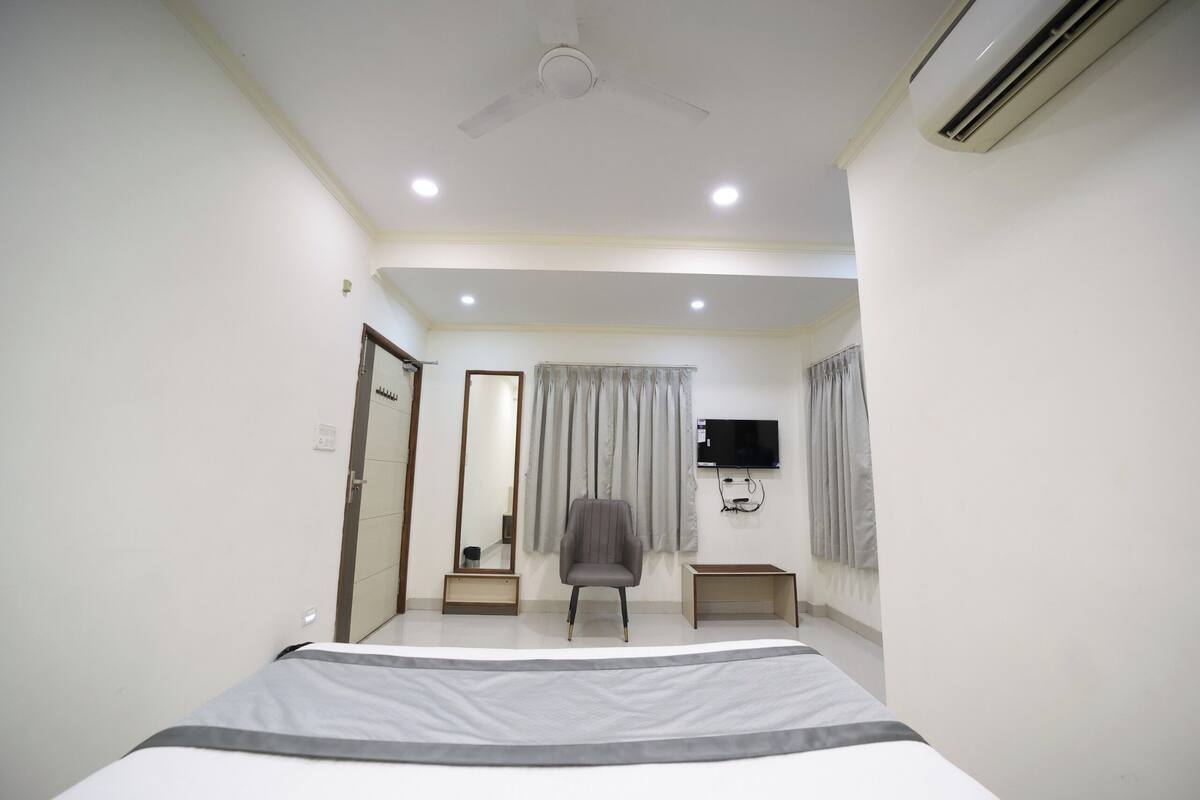 A bedroom with a bed, a chair, a TV, and an air conditioner.