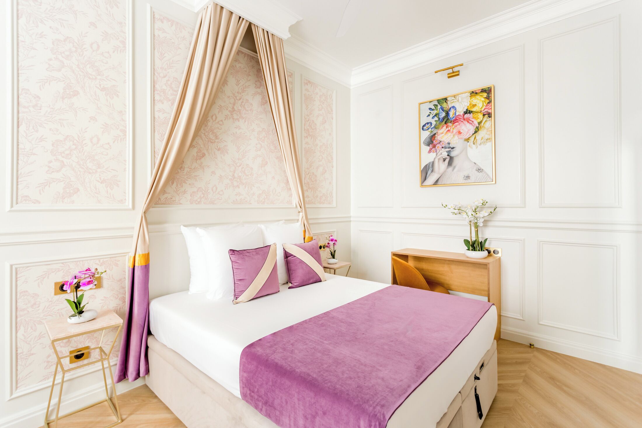 Une chambre à coucher bien aménagée, avec un lit à baldaquin, une table de chevet ornée d’un vase de fleurs et une œuvre d’art florale encadrée accrochée au mur.