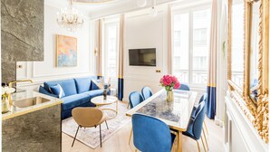 Un salon moderne avec un canapé bleu, une table à manger et un lustre.