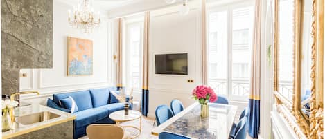 A modern living room with a blue sofa, a dining table, and a chandelier.