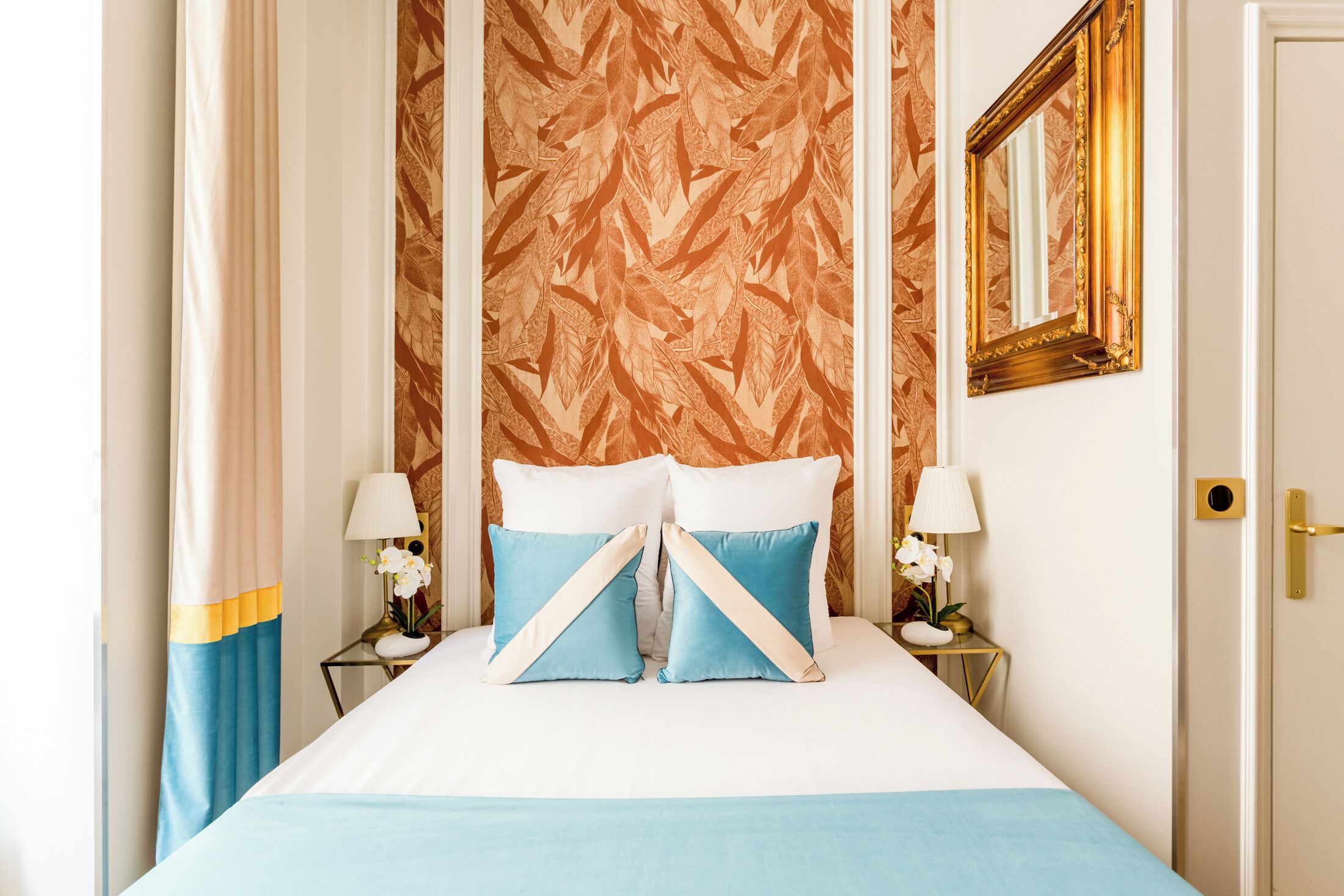 A bed with a white and blue bedspread, two nightstands with lamps, and a mirror on the wall.