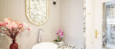 A bathroom with a marble vanity, a white sink, a large mirror with a gold frame, and two potted orchids.