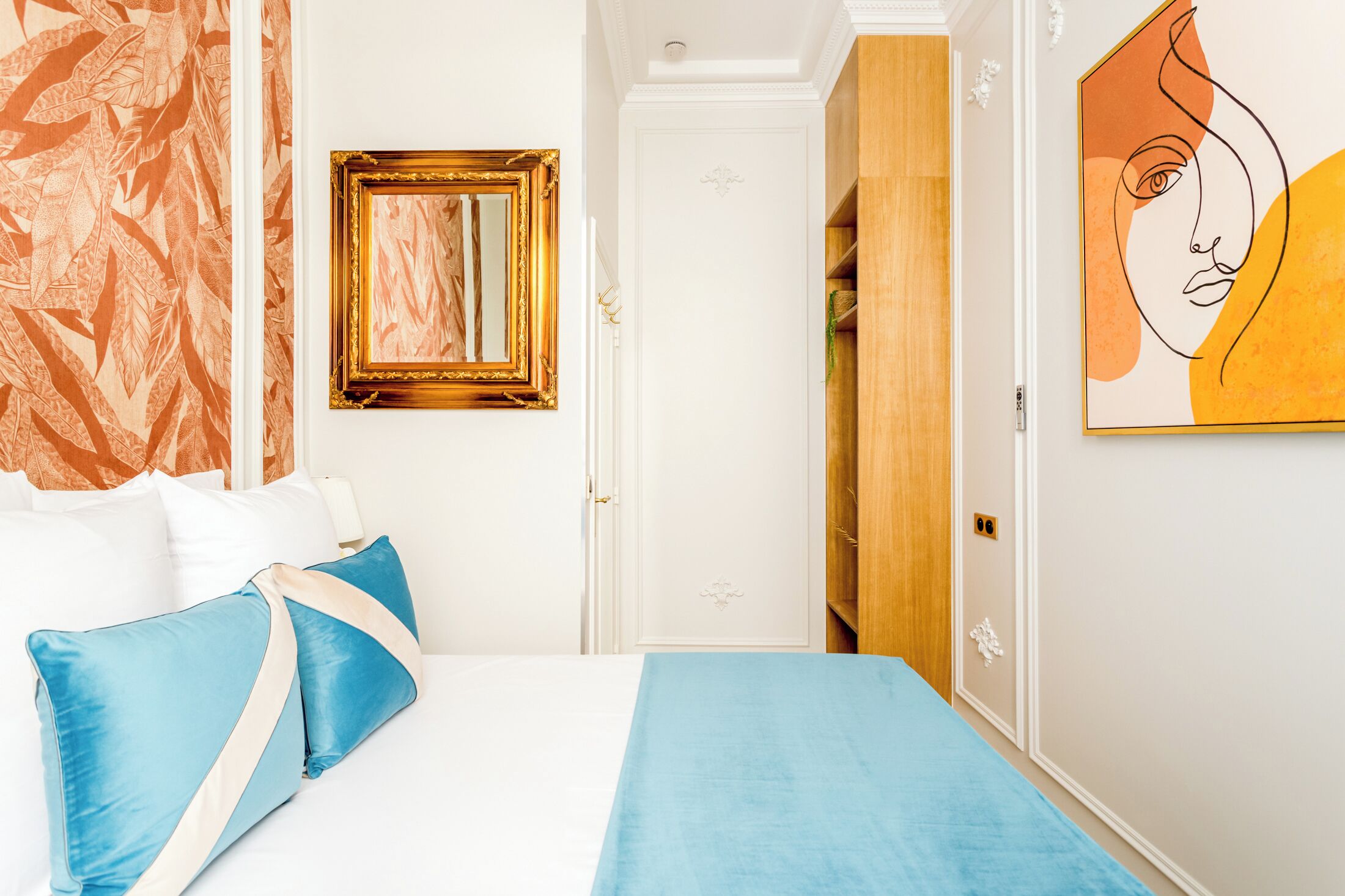 Ein Hotelzimmer mit Bett, Kissen, Spiegel, Tür und einem Bild an der Wand.