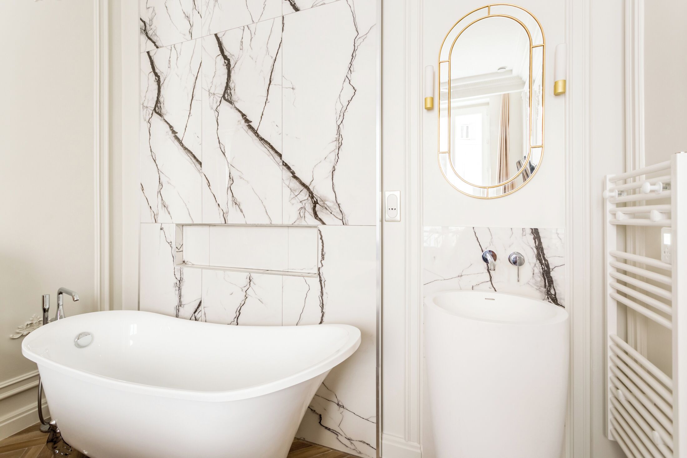 Une salle de bain avec une baignoire sur pieds, un lavabo sur colonne et un mur en marbre.