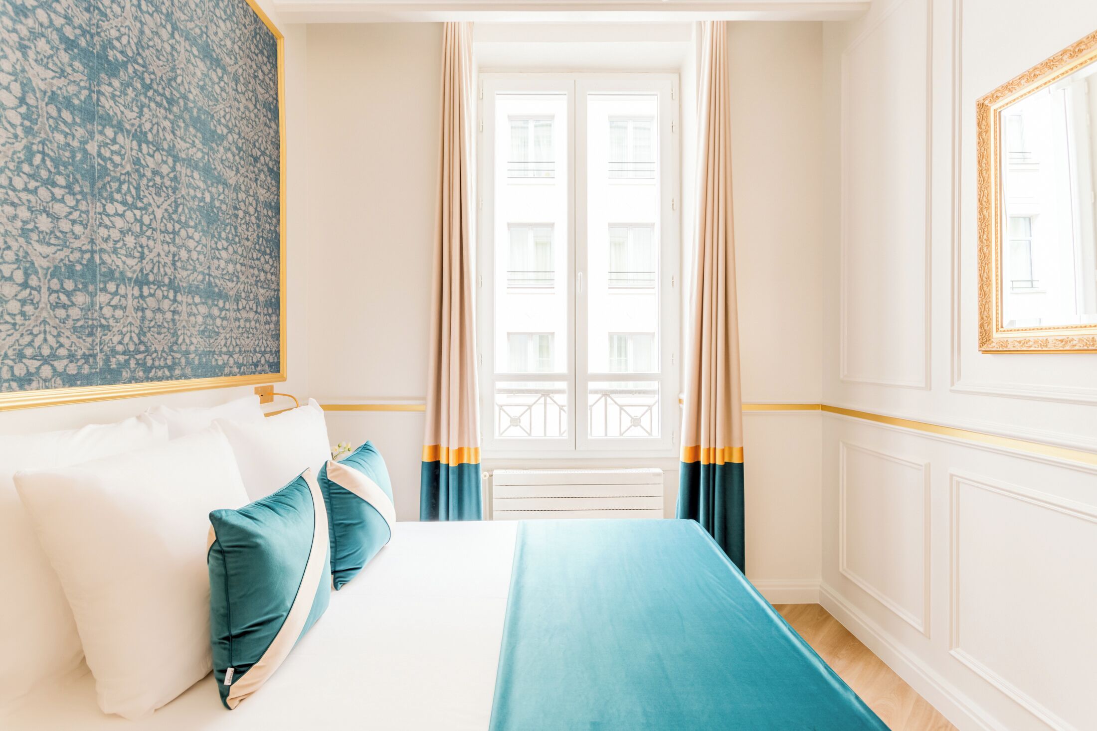 Une chambre d’hôtel avec un lit, une fenêtre avec des rideaux, un radiateur et un mur orné d’un motif.