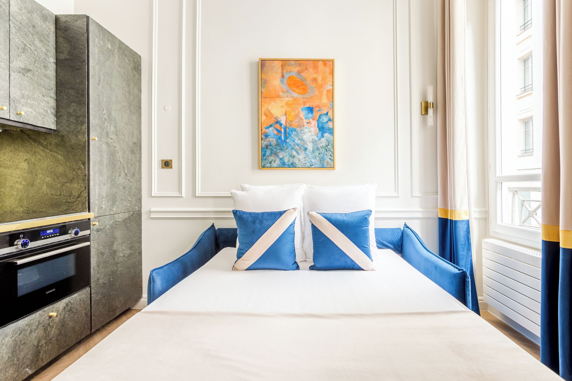 Una camera d'albergo con un letto, un quadro appeso al muro e un angolo cottura.