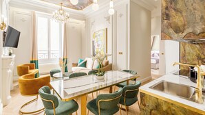 Un espace repas moderne avec une table en verre, des chaises recouvertes d’un tissu vert et un lustre.