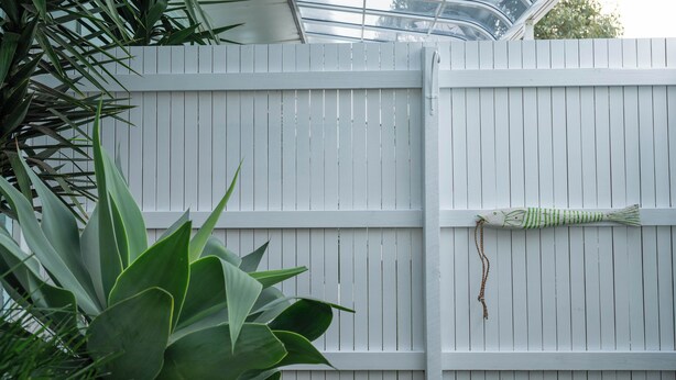 A white wooden fence with a green and white striped fish decoration hanging on it.