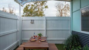 A wooden patio table with a glass enclosure, surrounded by a white fence, and a small potted plant.