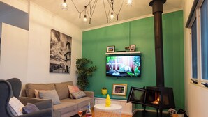 A living room with a green wall, a sofa, a TV, a fireplace, and a small table with a bottle and glass.