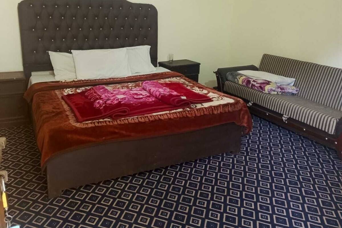 Ein ordentlich bezogenes Bett mit dunklem Kopfteil, einem gemusterten Boden, einem gestreiften Sofa und einem kleinen Fenster darüber.
