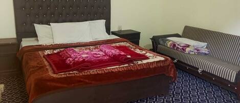 A neatly made bed with a dark headboard, a patterned floor, a striped sofa, and a small window above the bed.