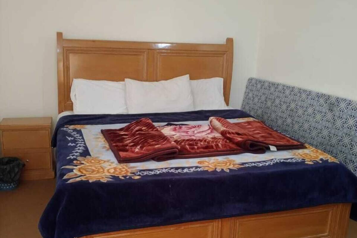 Ein Einzelbett mit Holz Kopfteil, einer blauen Bettdecke mit Blumenmuster und zwei roten Kissen.