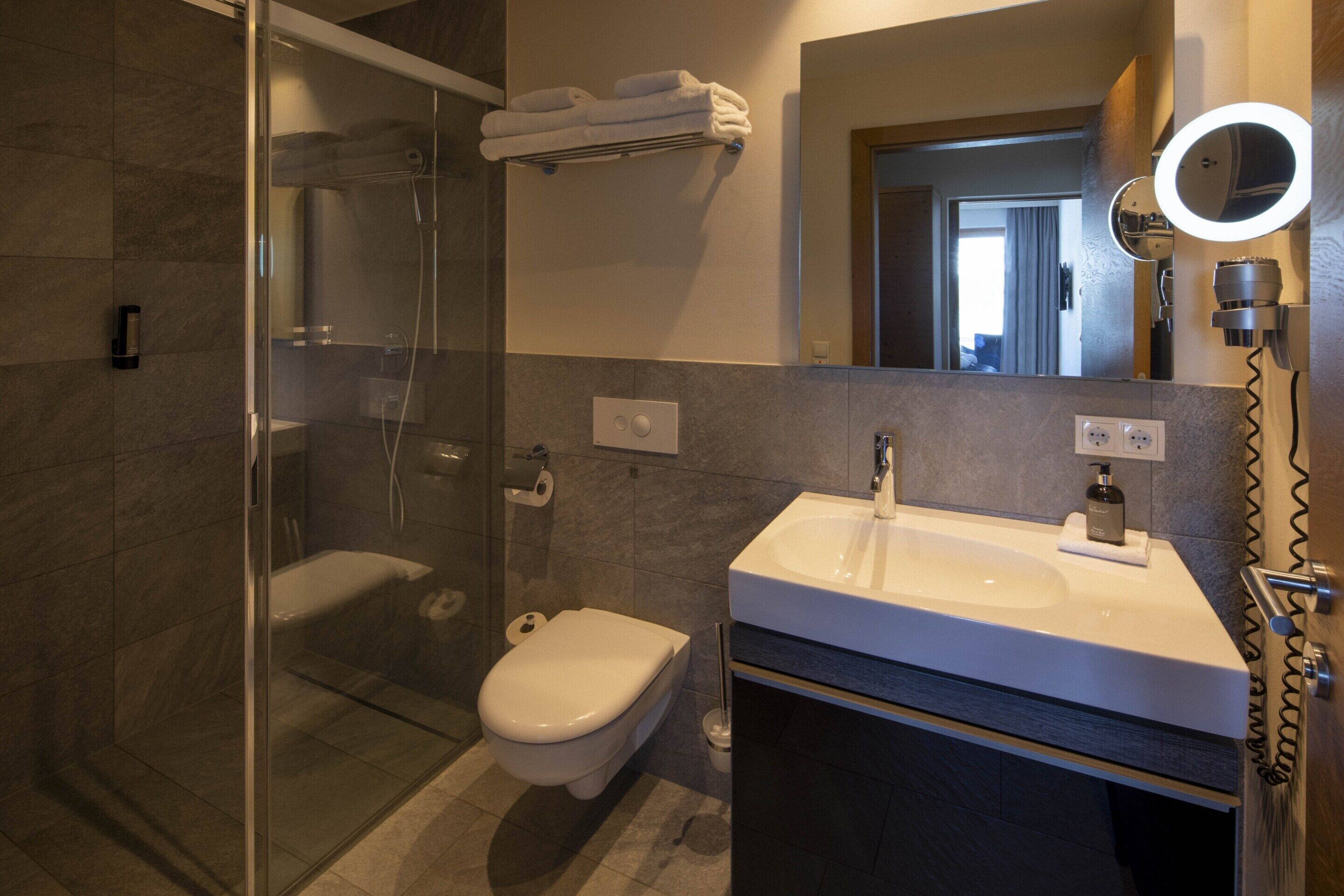 A modern bathroom with a glass-enclosed shower, a toilet, a sink with a mirror, and a towel rack.