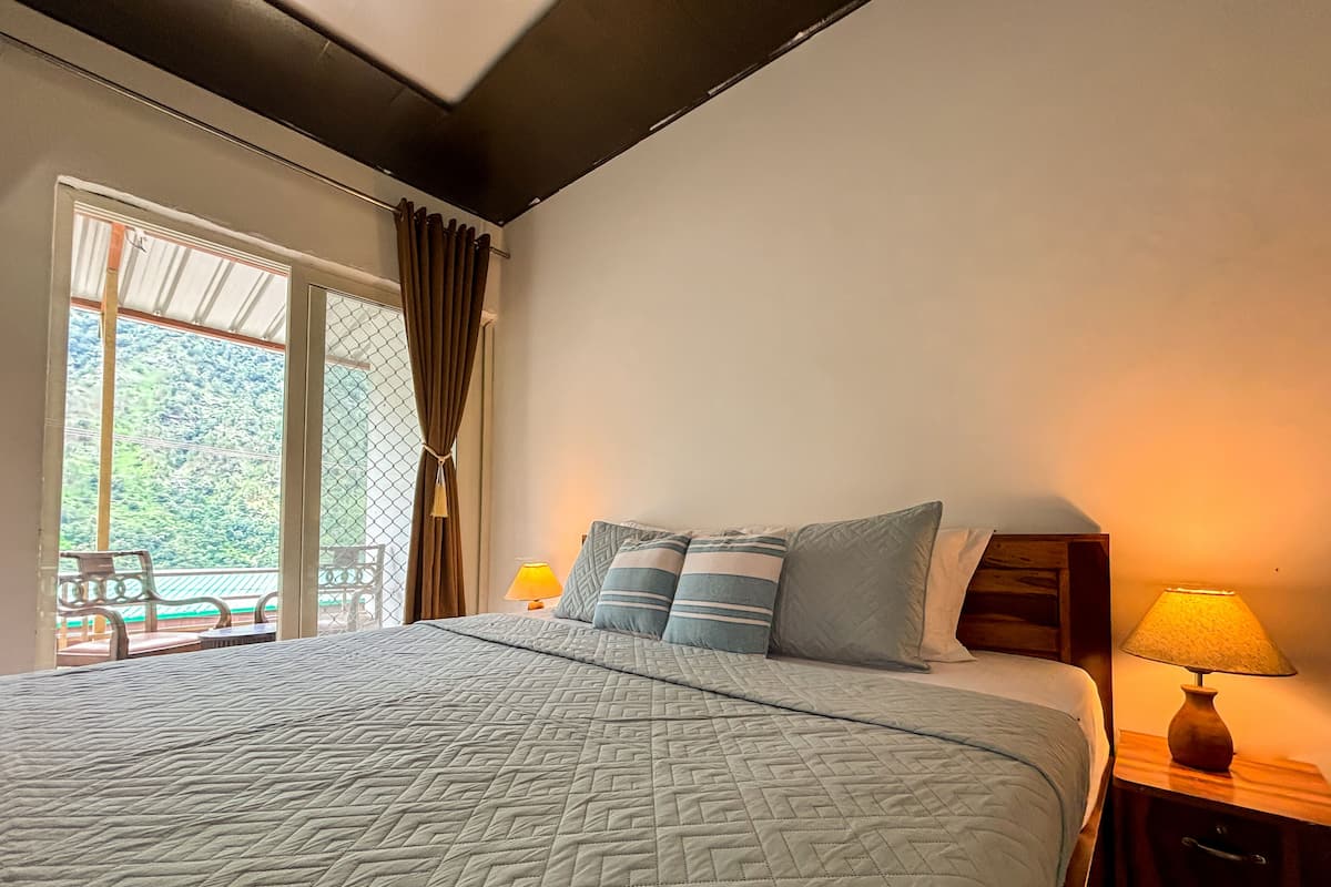 Un dormitorio con una cama grande, dos lámparas de noche, un ventanal con cortinas y vistas al exterior.