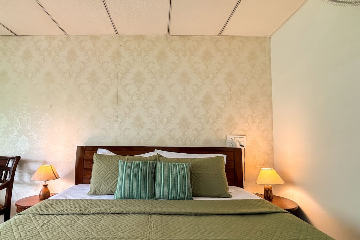 Habitación de hotel con cama, dos lámparas de noche, cabecero de madera y papel tapiz estampado.
