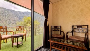 Un balcón con una mesa y sillas de vidrio, con vistas a un paisaje montañoso.