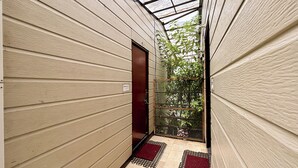 Un pasillo estrecho con paneles de madera y techo de cristal, que conduce a una puerta y un portón con vegetación al exterior.