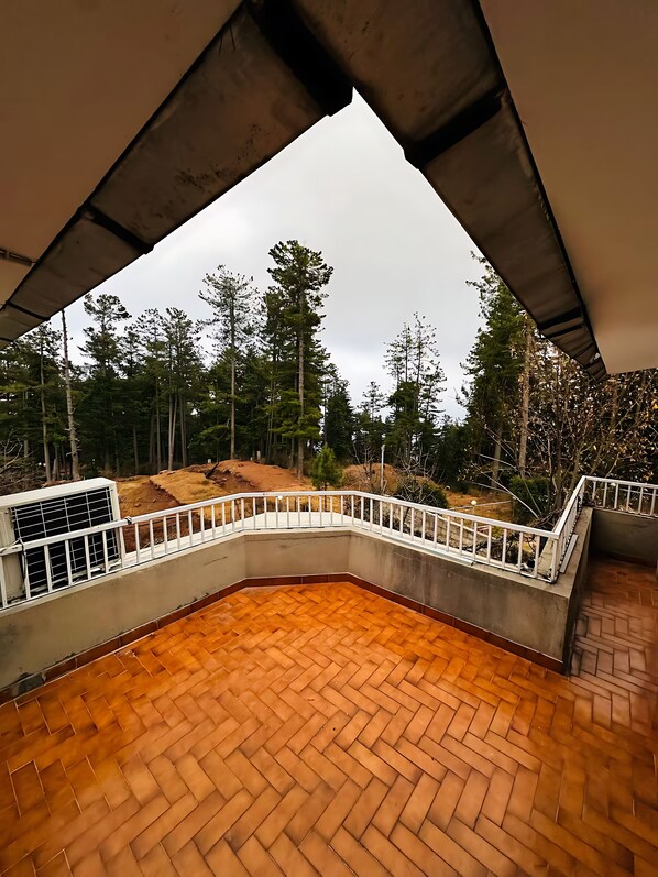 A covered outdoor area with a wooden floor and white railing, overlooking a forested landscape.