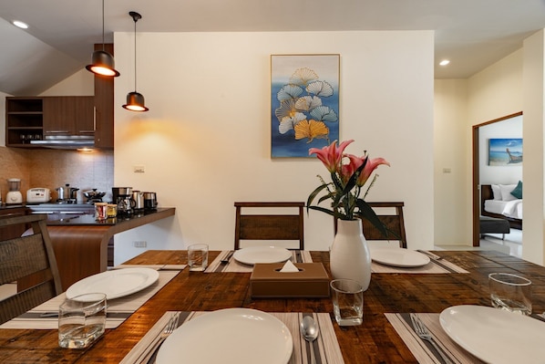 Un comedor con una mesa de madera dispuesta para cuatro personas, un florero con flores y un cuadro en la pared.