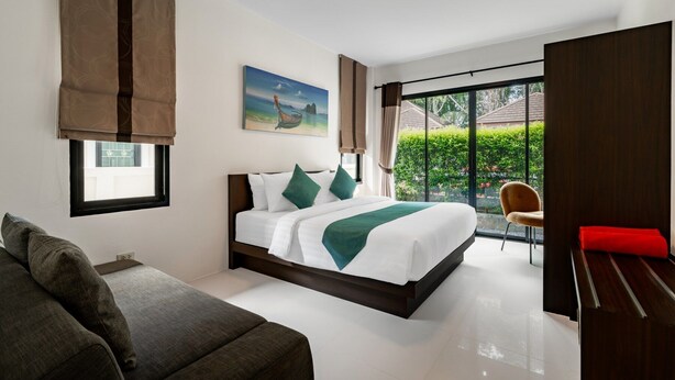 A modern hotel room with a large bed, a sofa, a desk, and a view of greenery outside.