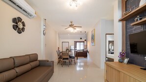 A modern living room with a sofa, dining area, kitchen, and a TV on a wooden cabinet.