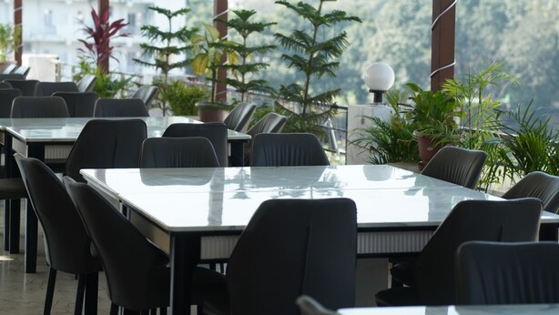 Un ristorante con tavoli e sedie, ampie finestre e piante in vaso.