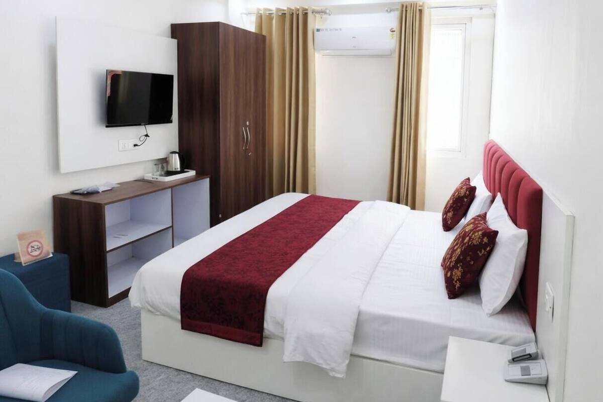 A hotel room with a bed, a TV mounted on the wall, a desk, and a wardrobe.