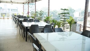 Un'ampia sala da pranzo con tavoli e sedie in marmo, ampie finestre che offrono vista sulla città e piante in vaso.