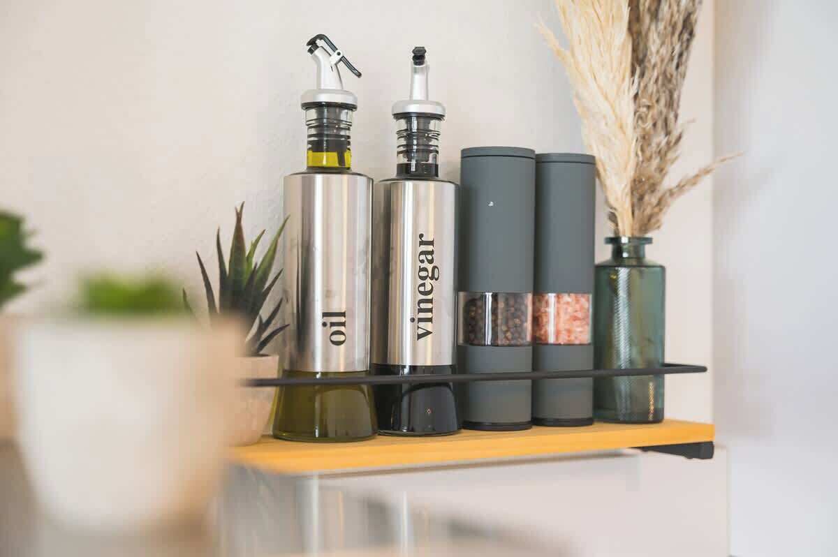 A shelf with three bottles labeled 'oil' and 'vinegar', and a small vase with dried plants.