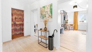 Et moderne interiør med trægulv, et bord i sort metal med en vase og en paraply, et kort på væggen og udsigt udendørs gennem et vindue.