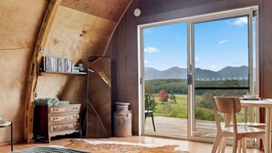 A cozy room with a wooden ceiling, a large sliding glass door leading to an outdoor deck, a rustic dresser, and a woven rug. - Bickell's Hut - Off-Grid Farm Stay, Fire Pit, Fire Bath, Cozy, Views - Sleeps 2 -4 (Hydes Creek)