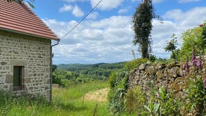A stone house with a red roof, surrounded by lush greenery and a stone wall.
